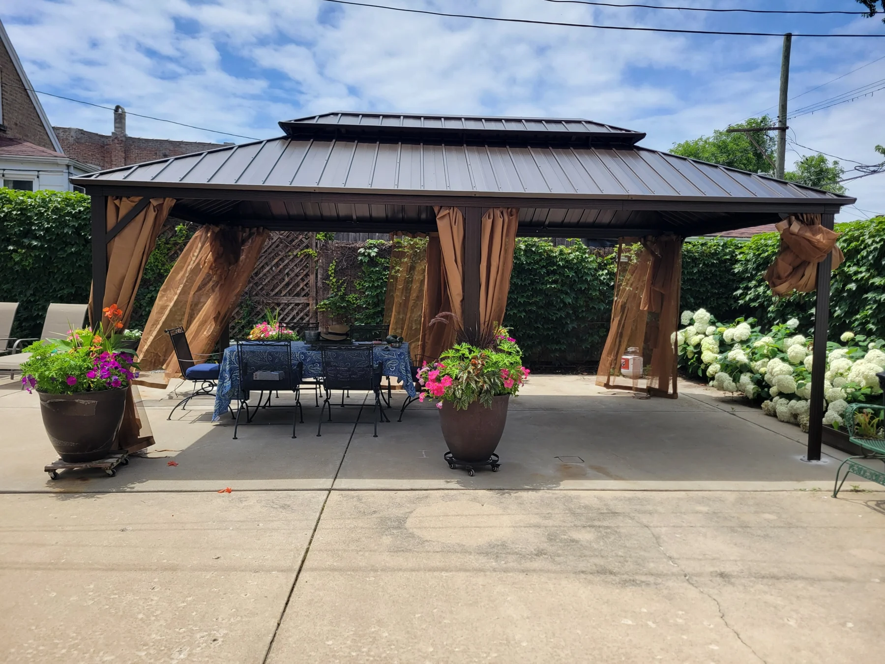 After assembly: a wide view of the gazebo with its hardtop roof and curtains, framing the patio seating and flower planters.