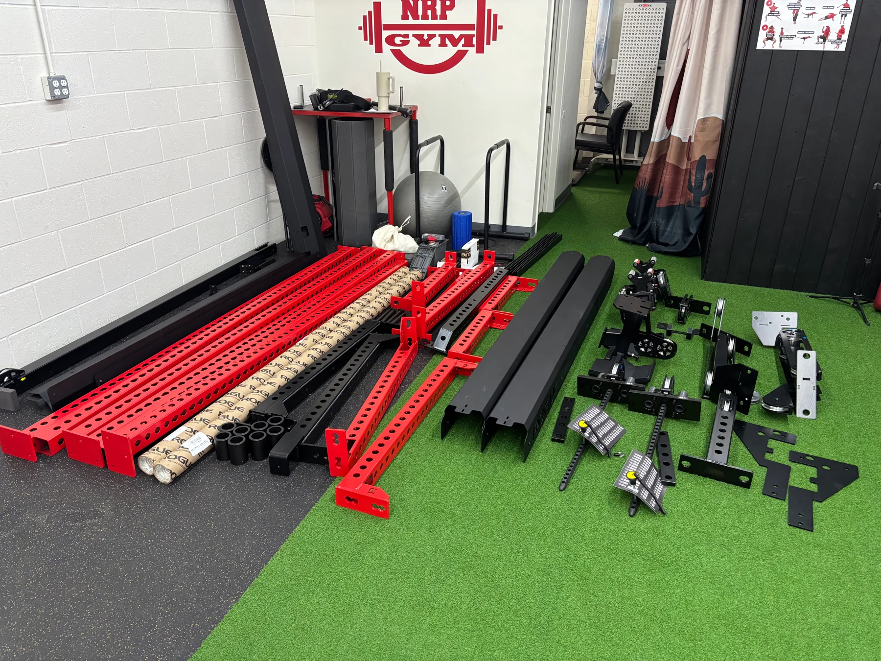 Before assembly: red uprights, black frame sections, brackets, and hardware laid out for the build.